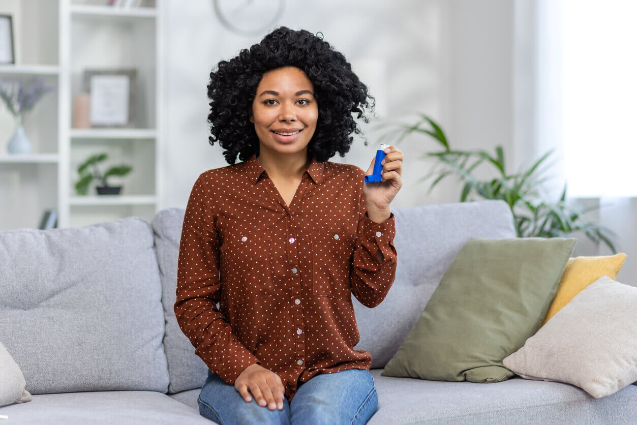 Image of an asthmatic woman sitting at home on the couch, holding and showing her asthma inhaler.